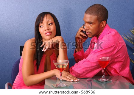 African American couple in a martini bar.Man talking on cell phone while the woman sits by annoyed and bored