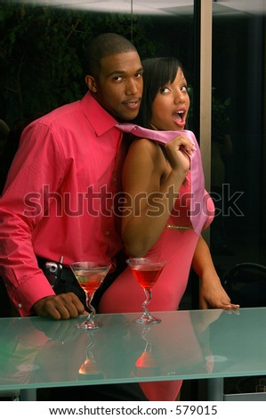 African American couple in a martini bar.Man being lead off playfull by woman pulling his necktie