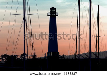 Long Beach Harbor Lighthouse back lit and silhouetted by a Southern California sunset and framed by the tall masts of Sail Boats