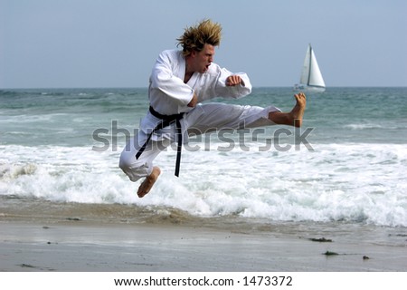 Man with a black belt working out on the beach. Executing a flying kick
