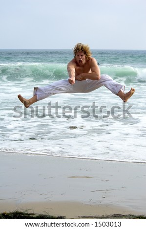 Man with a black belt working out on the beach. Executing a flying kick