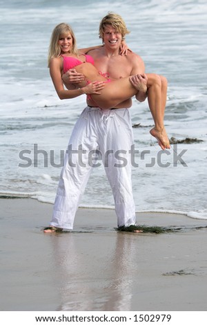 A man carrying a pretty blond out of the water at the beach