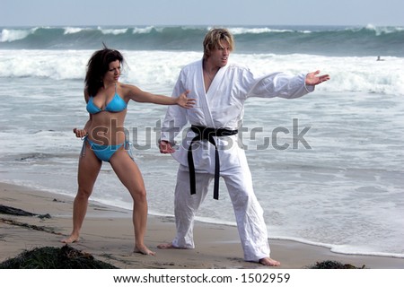 Man with a black belt teaching a woman martial arts on the beach