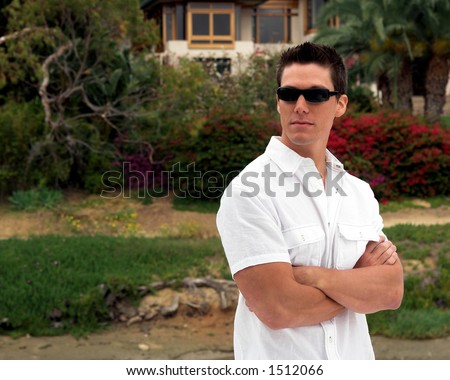 A stylish and confident young man in a white button down shirt and dark sunglasses standing with his arms crossed