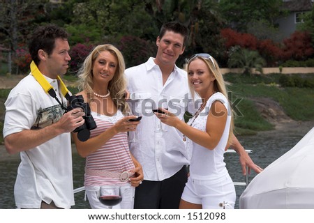 Two young couples drinking a glass of wine on a private yacht and looking out to sea with binoculars as they pull out of the harbor