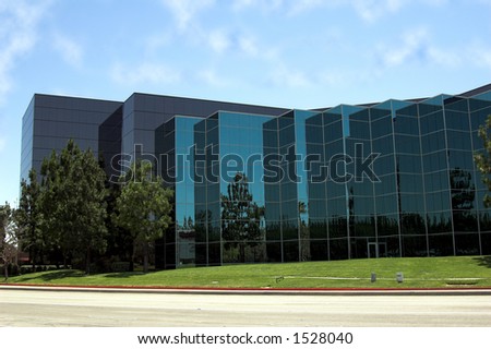 Modern corporate office building in Southern California built of reflective blue glass. Nicely landscaped with grass and evergreen trees