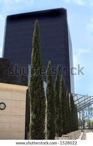 Modern corporate office building in Southern California built of reflective black glass. Nicely landscaped with stainless steel pillars and evergreen trees