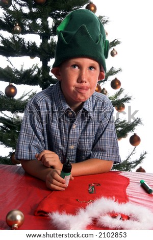 A perplexed young elf working on a Christmas craft project of decorating a stocking rolls his eyes and licks his lips
