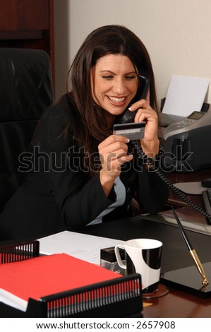 Happy business woman on her office phone and using a credit card to pay for a purchase