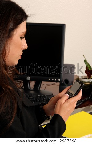 Over the shoulder view of a female executive typing a text message on her cell phone while sitting at her desk