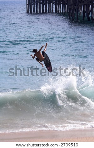 Young man on a  skimboard gets huge air but looses contact with his board after cutting up the face of the receding surf  near Balboa Pier,  Balboa Beach California.