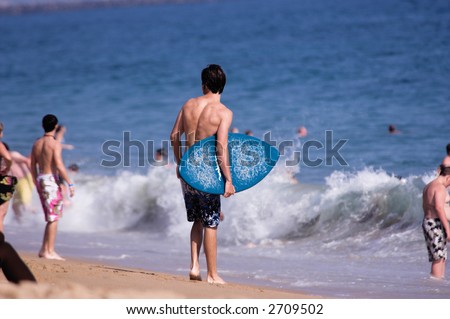 Young man with a skimboard assesses the surf conditions on a crowded Balboa Beach. Balboa California