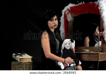Beautiful raven haired Gothic Vampire Slayer in a black and grey dress and striking green eyes. sitting at her vanity with her doll on her lap.