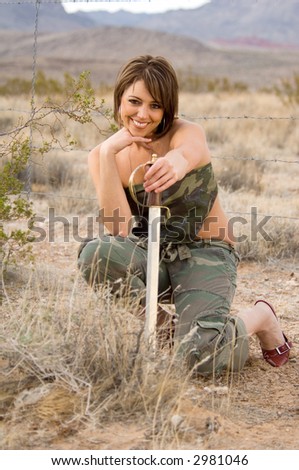 Portrait of a woman in the desert crouched behind a bush in the desert holding a sword