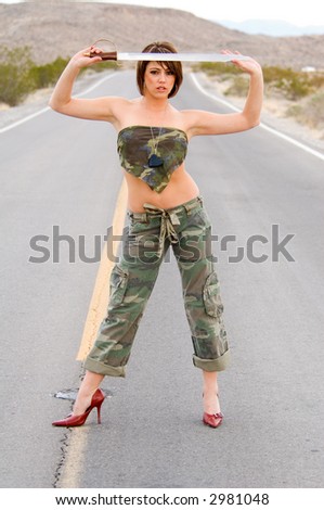 Portrait of a woman with a sword over her head in fatigues in the desert