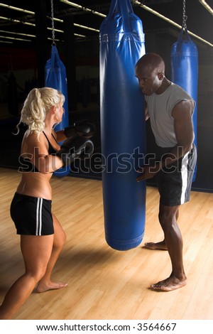 Beautiful but dangerous female fighter working with her trainer punching a heavy bag in an Mixed Martial Arts gym.