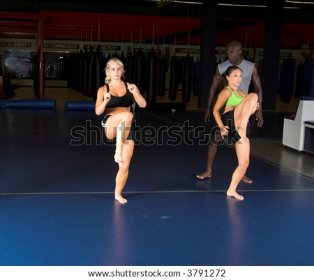 Young female MMA fighters working on high knee kicks with their personal trainer in the gym