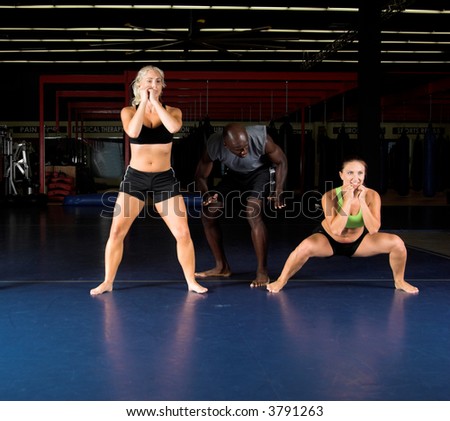 Young female MMA fighters doing power squats in the gym with their trainer.  Focus on on the right in a deep squat