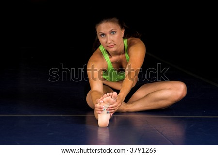 Attractive brunette MMA Fighter stretching out during a warm up in a boxing gym