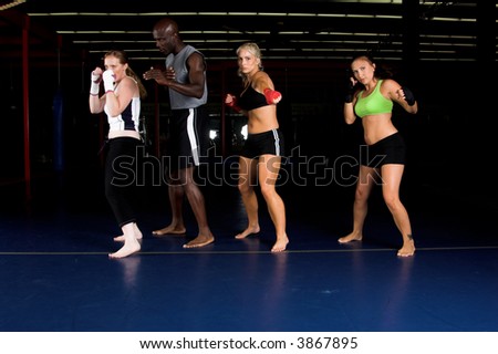 Three beautiful young woman fighters shadow boxing with their trainer in an MMA gym