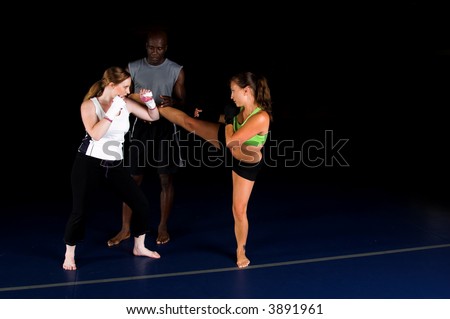 Young female MMA fighters working on high head kicks with their personal trainer in the gym