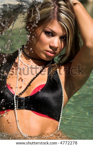 Sexy Caucasian woman wearing a black and pink bikini and wading in a swimming pool near a small waterfall