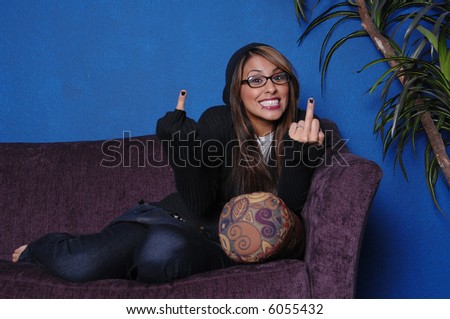 A maniacal looking woman on a purple couch in a blue room giving the camera double middle fingers