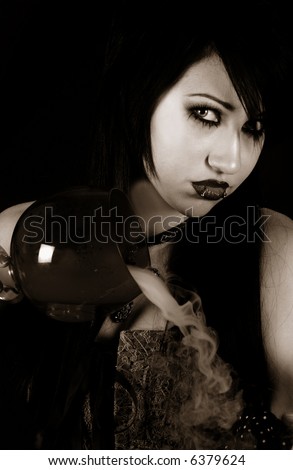 Beautiful raven haired gothic Vampire girl in a black and grey dress pouring steaming Witch\'s Brew from a Red Goblet