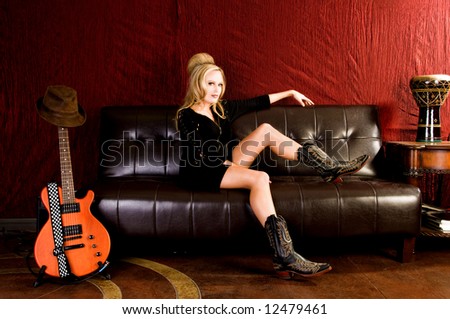 Beautiful young woman sitting on a leather couch in a black knit dress and cowboy boots