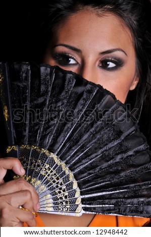 beautiful multi ethnic woman of asian and hispanic descent behind a black fan on a black background