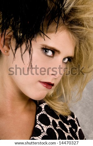 Young blonde woman with big teased hair, a small clutch and a feather hair piece against a concrete wall