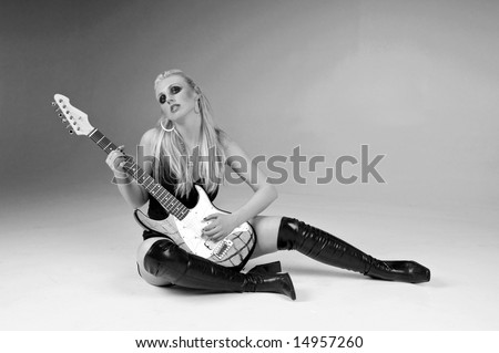 Pretty blonde in black shorts, pinstripe and lace vest and thigh high boots sitting on the floor with an electric guitar