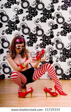 Young woman sitting on a dance studio floor in tights and a red bra and playing with red high heels