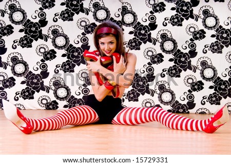 Young woman sitting on a dance studio floor in tights and a red bra  and playing with red high heels