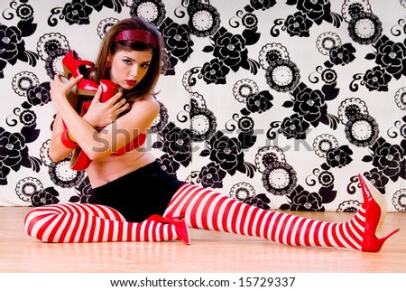 Young woman sitting on a dance studio floor in tights and a red bra and playing with red high heels
