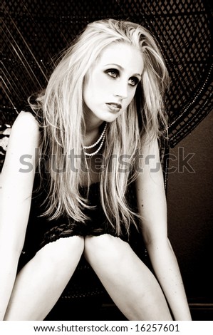 A beautiful young fashion model with long blond hair in a black cocktail dress sitting slumped in a wicker chair