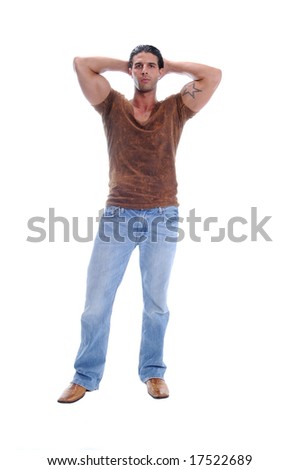 Muscular young man standing in jeans and a brown V neck tee shirt with his arms raised and hands behind his head