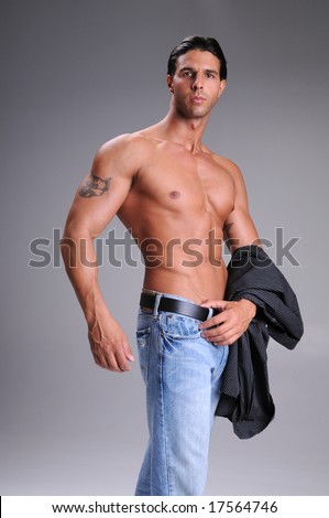 Muscular young man standing bare chested in jeans with a black long sleeve dress shirt over his arm