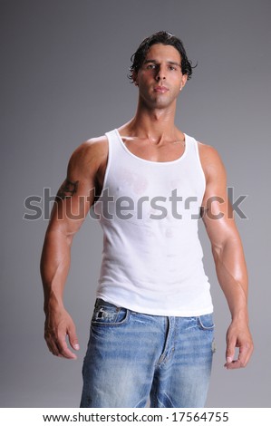 Muscular young man standing in jeans and a white wife beater tee shirt