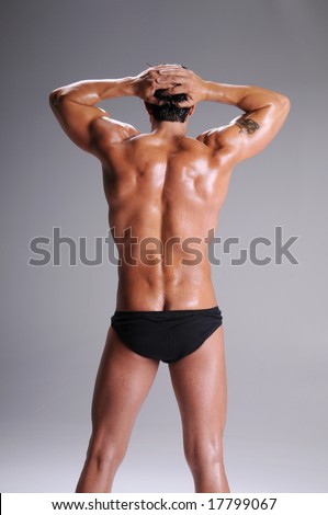 Rear view of a muscular young man standing bare chested in black brief style underwear