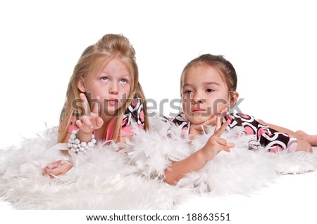 Little blonde haired girl laying on the floor in a pastel polka dot dress and a white feather boa with a white pearl bracelet on her arm with her little sister