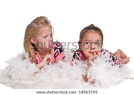 Little blonde haired girl laying on the floor in a pastel polka dot dress and a white feather boa with a white pearl bracelet on her arm with her little sister