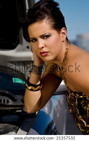 Beautiful young Italian woman stranded along the road with a broke down car wearing a fashionable black and gold party dress