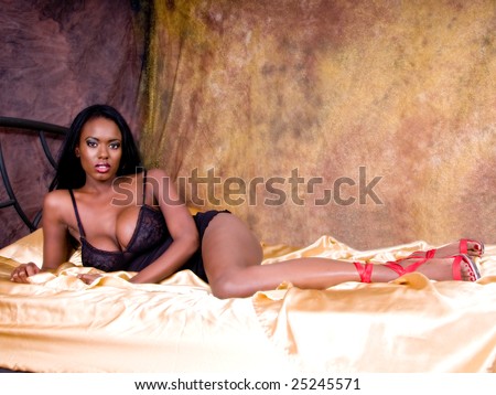 Sexy African American woman with very large breasts looking lovely in black lingerie  in a gold bedroom