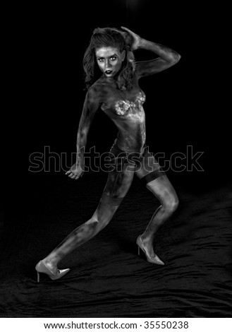 Sexy body painted female zombie standing on red velvet in a black room