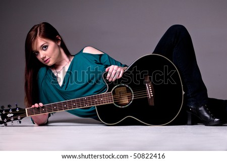 Pretty young redheaded guitar player standing with her acoustic guitar