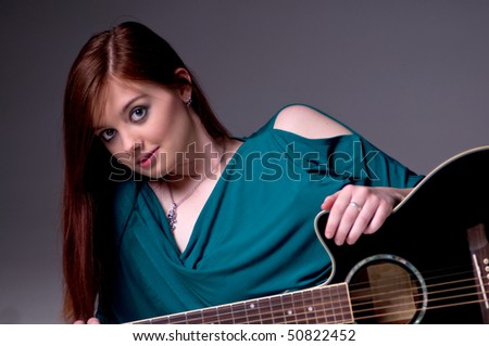 Pretty young redheaded guitar player laying on her side with her acoustic guitar