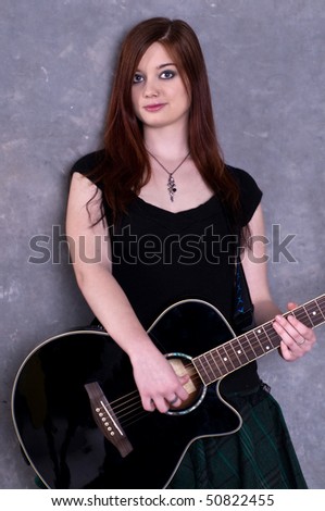 Pretty young redheaded guitar player standing with her acoustic guitar