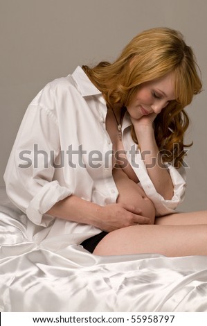 Happy red haired woman 8 months pregnant laying on the bed in a mans dress shirt and panties