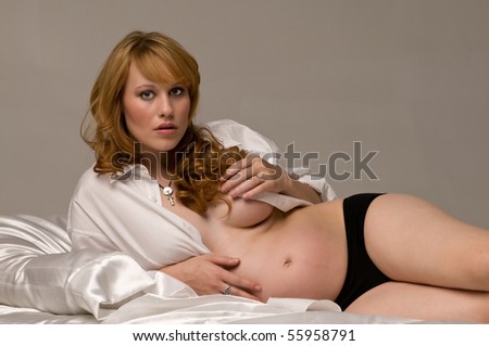 Beautiful red haired woman 8 months pregnant laying on the bed in a mans dress shirt and panties